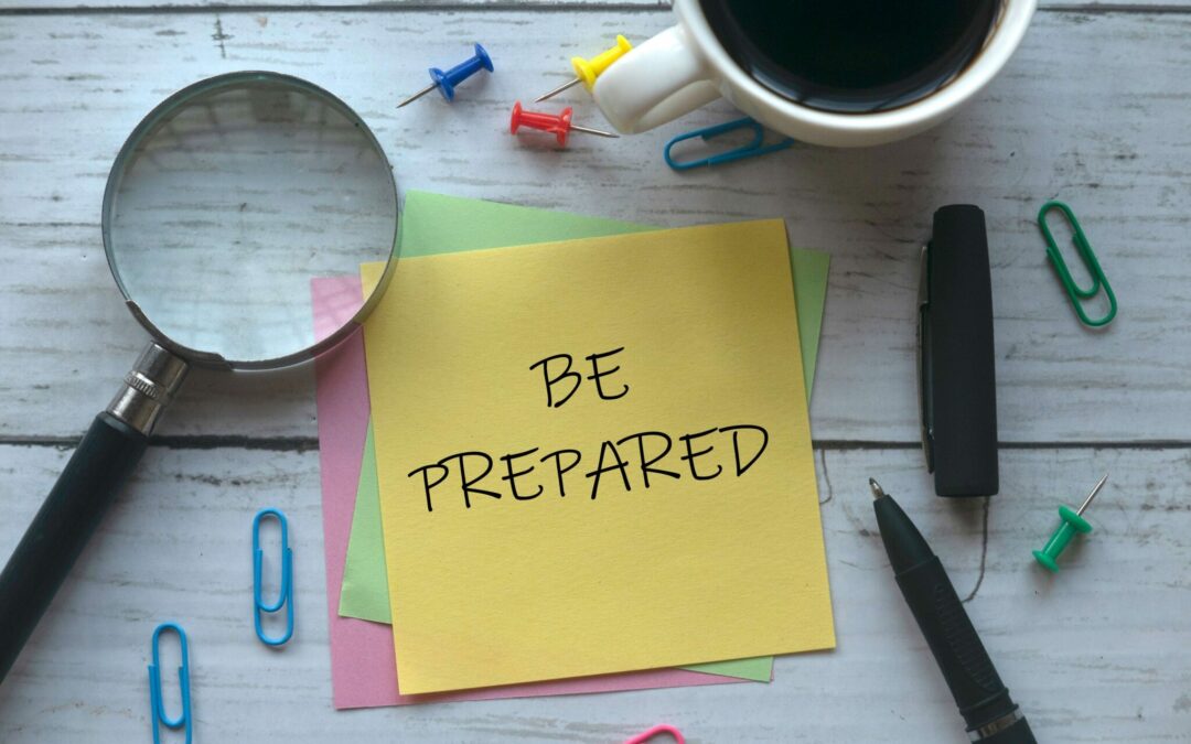 yellow sticky note with "be prepared" written on it with various office items around it