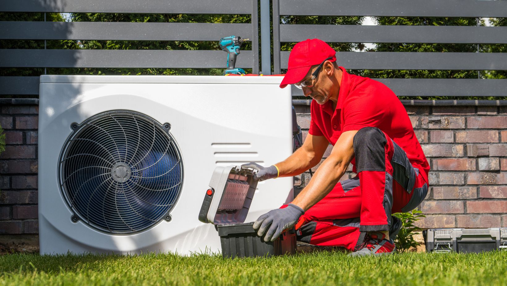 Untitled design (2) A man in red shirt and hat fixing an air conditioner.